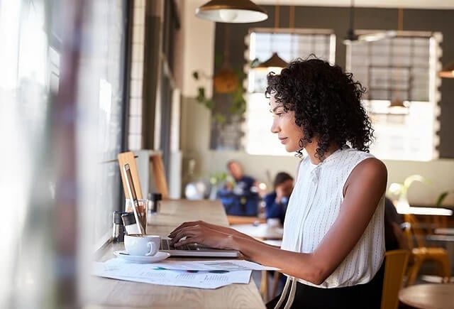 Businesswoman By Window Working On Laptop In Coffee Shop