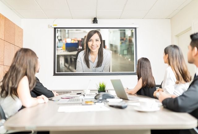 business people looking at blank projection screen while sitting at conference table