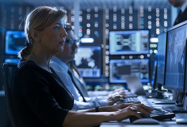 Female Government Employee Works in a Monitoring Room. In The Background Supervisor Holds Briefing. Possibly Government Agency Conducts Investigation.