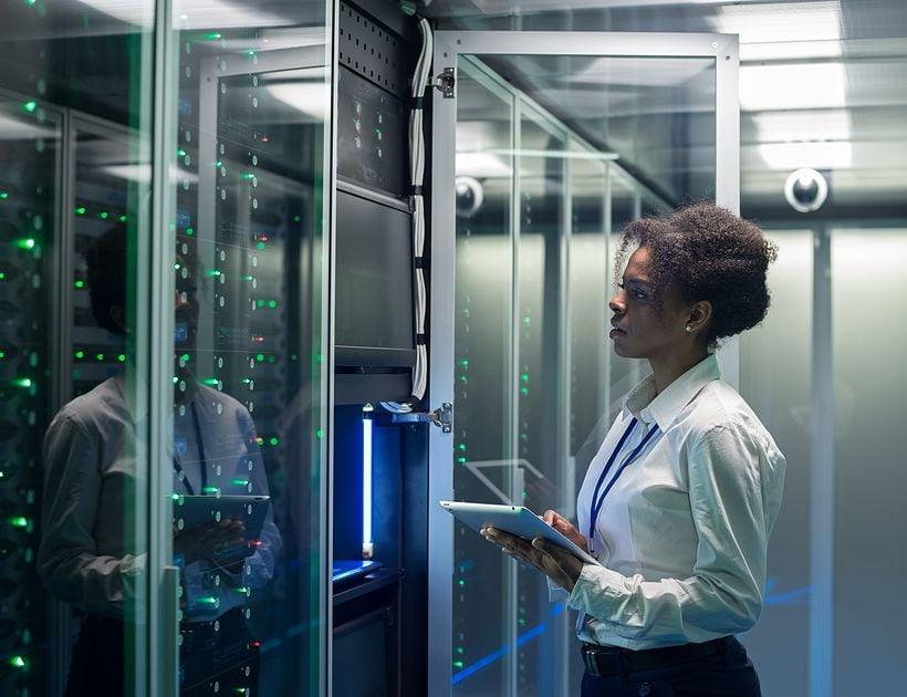 Medium shot of female technician working on a tablet in a data center full of rack servers running diagnostics and maintenance on the system