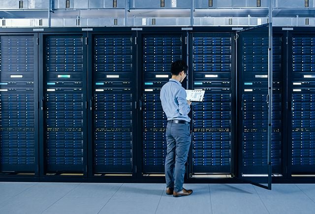 IT Engineer Standing Beside Open Server Rack Cabinets, Does Wireless Maintenance and Diagnostics Procedure with a Laptop.