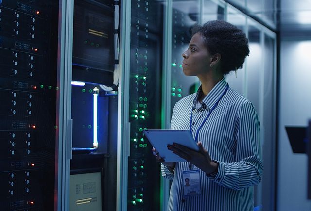 Portrait of African American woman working as IT engineer and standing among server racks in data center room