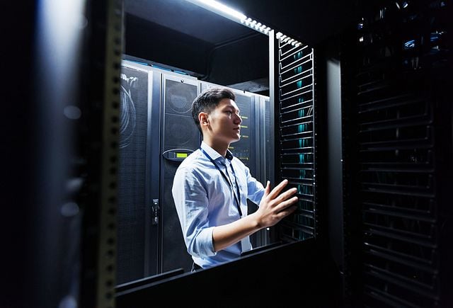 Young IT engineer inspecting data center servers.